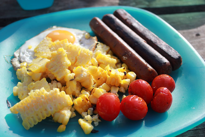 Camping breakfast, with meatless sausages, corn, tomatoes, and sunny side up.